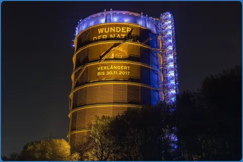 Beleuchteter Gasometer mit Werbung für Ausstellung