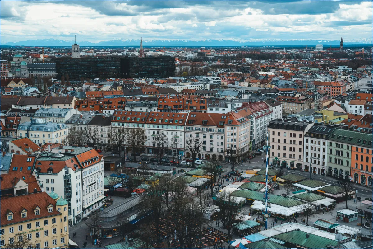 Stadtansicht mit Marktplatz und Bergen im Hintergrund.