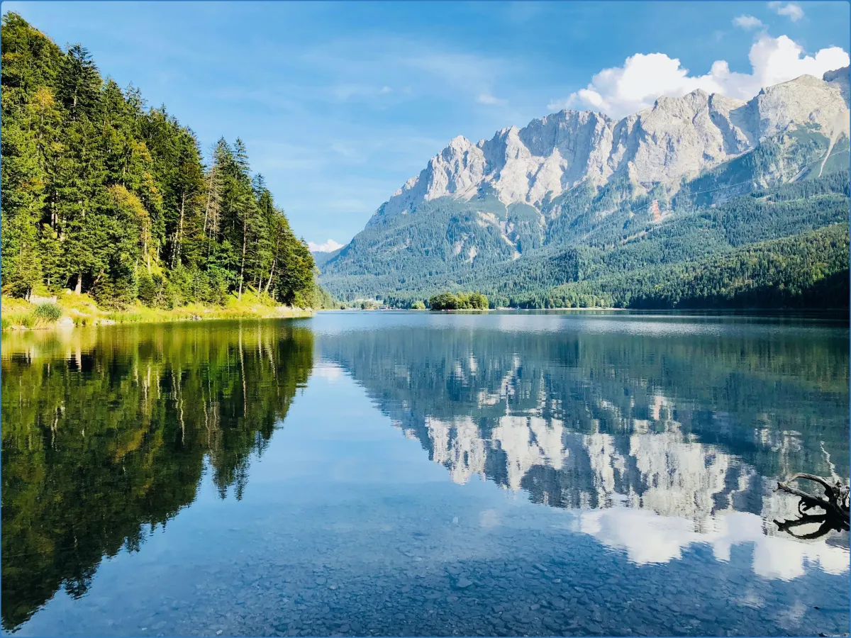 Bergsee mit Wald und Bergen im Hintergrund.