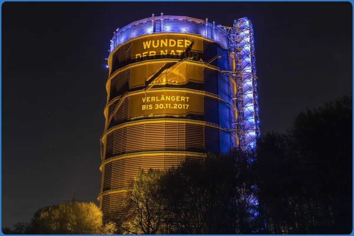 Beleuchteter Gasometer mit Werbung für Ausstellung
