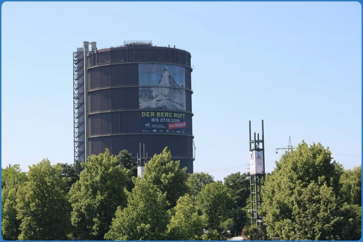 Gasometer mit Plakat 'Der Berg ruft' umgeben von Bäumen