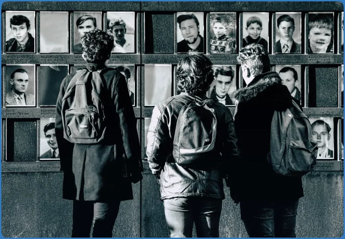 Drei Personen betrachten eine Fotowand.