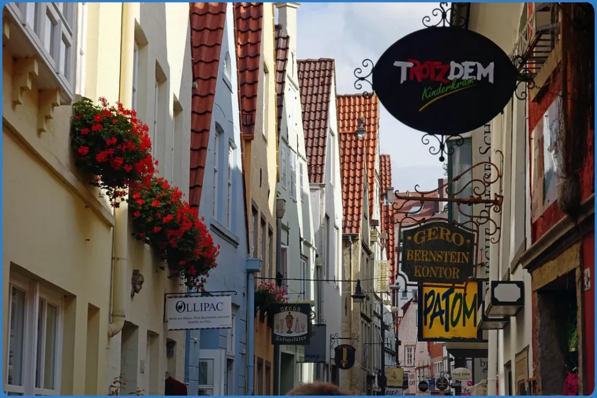 Schmale Gasse mit Fachwerkhäusern und Schildern.