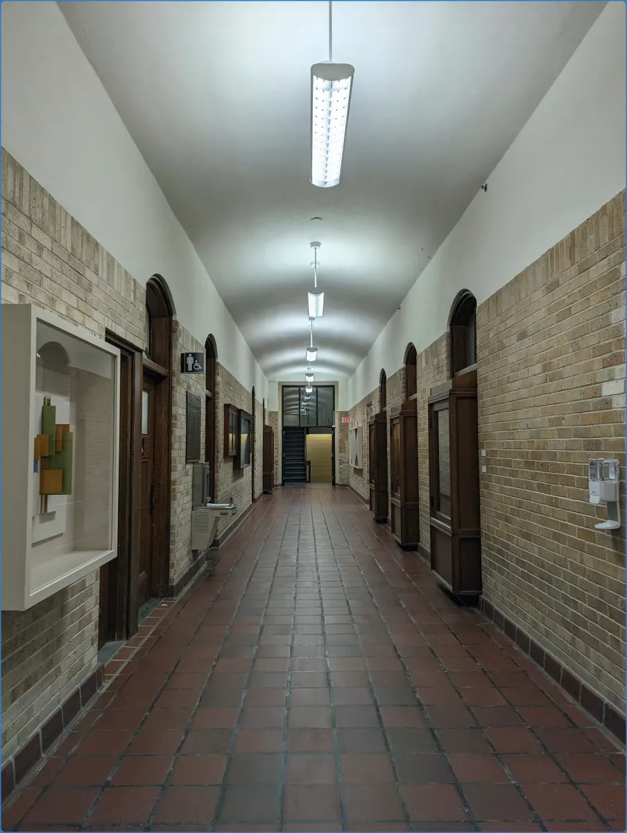 Langer Flur mit Backsteinwänden und Deckenbeleuchtung.