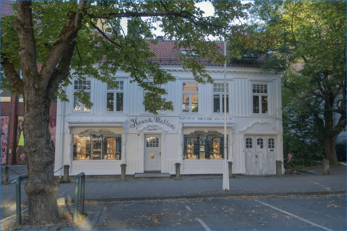 Weißes Gebäude mit Schaufenstern und Bäumen davor.