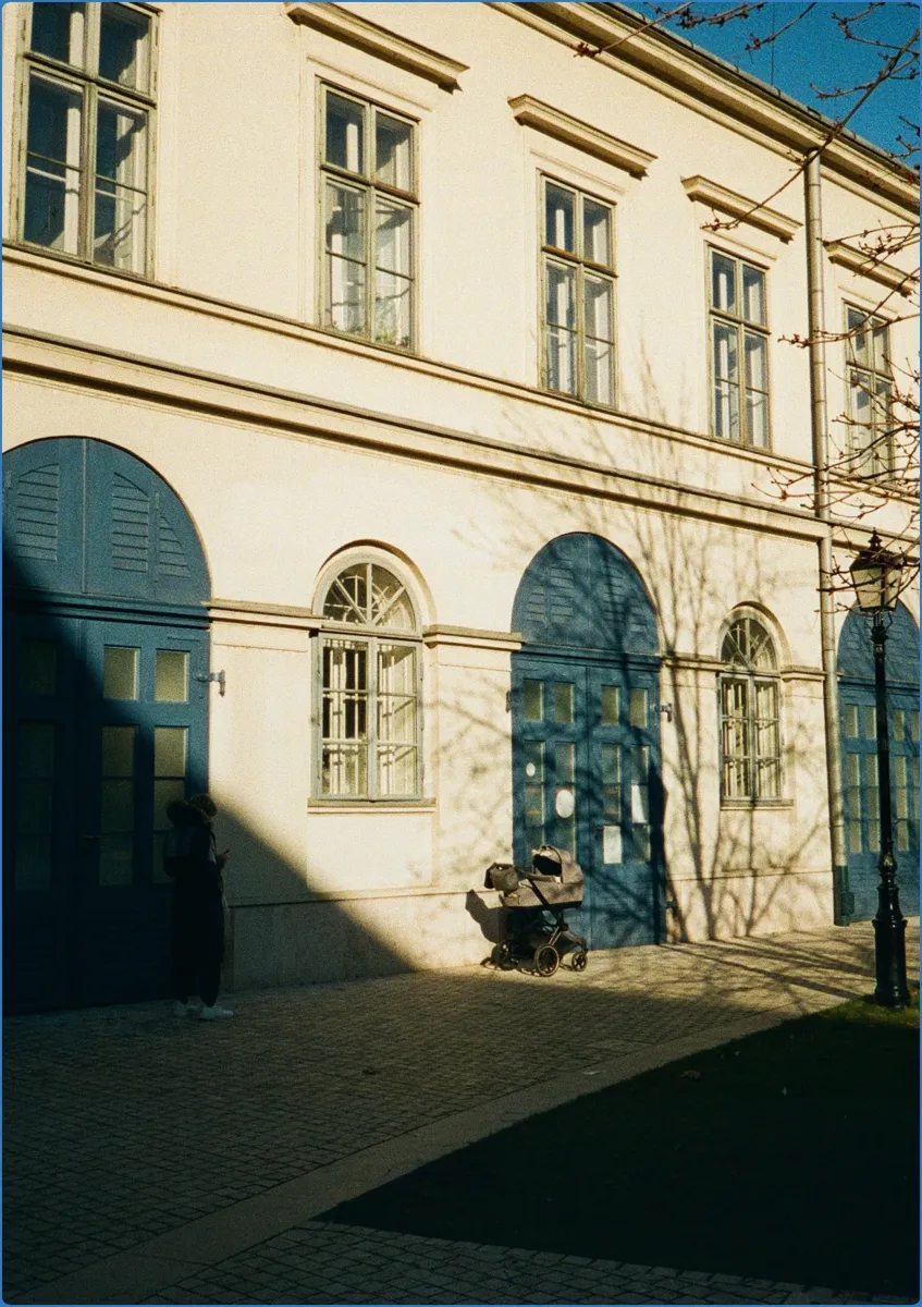 Gebäude mit blauen Türen und Kinderwagen im Schatten.