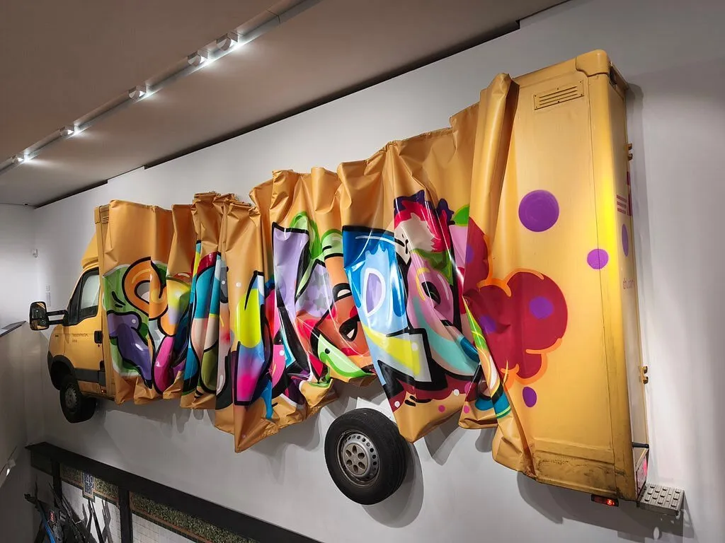 Gelbes Fahrzeug mit buntem Graffiti an der Wand.