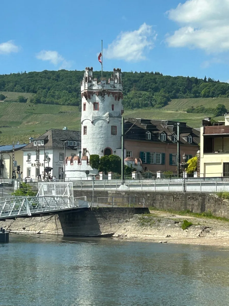 Weißer Turm am Flussufer mit Hügel im Hintergrund.