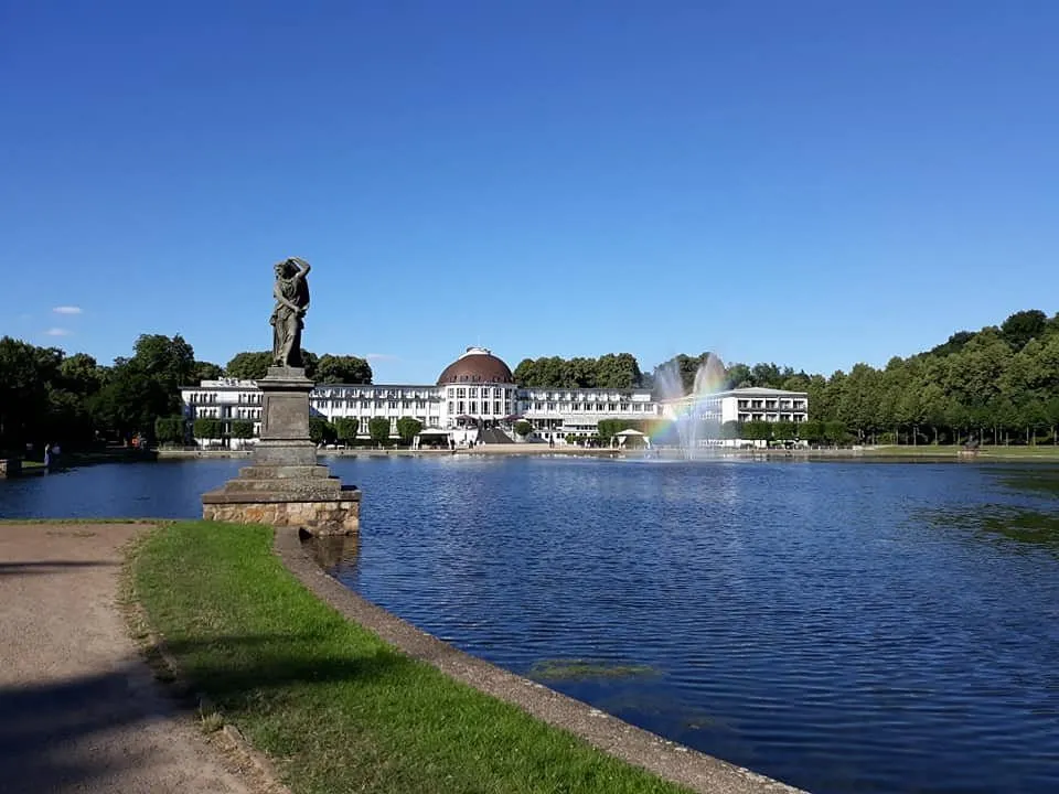 Statue und Gebäude am See mit Regenbogen.