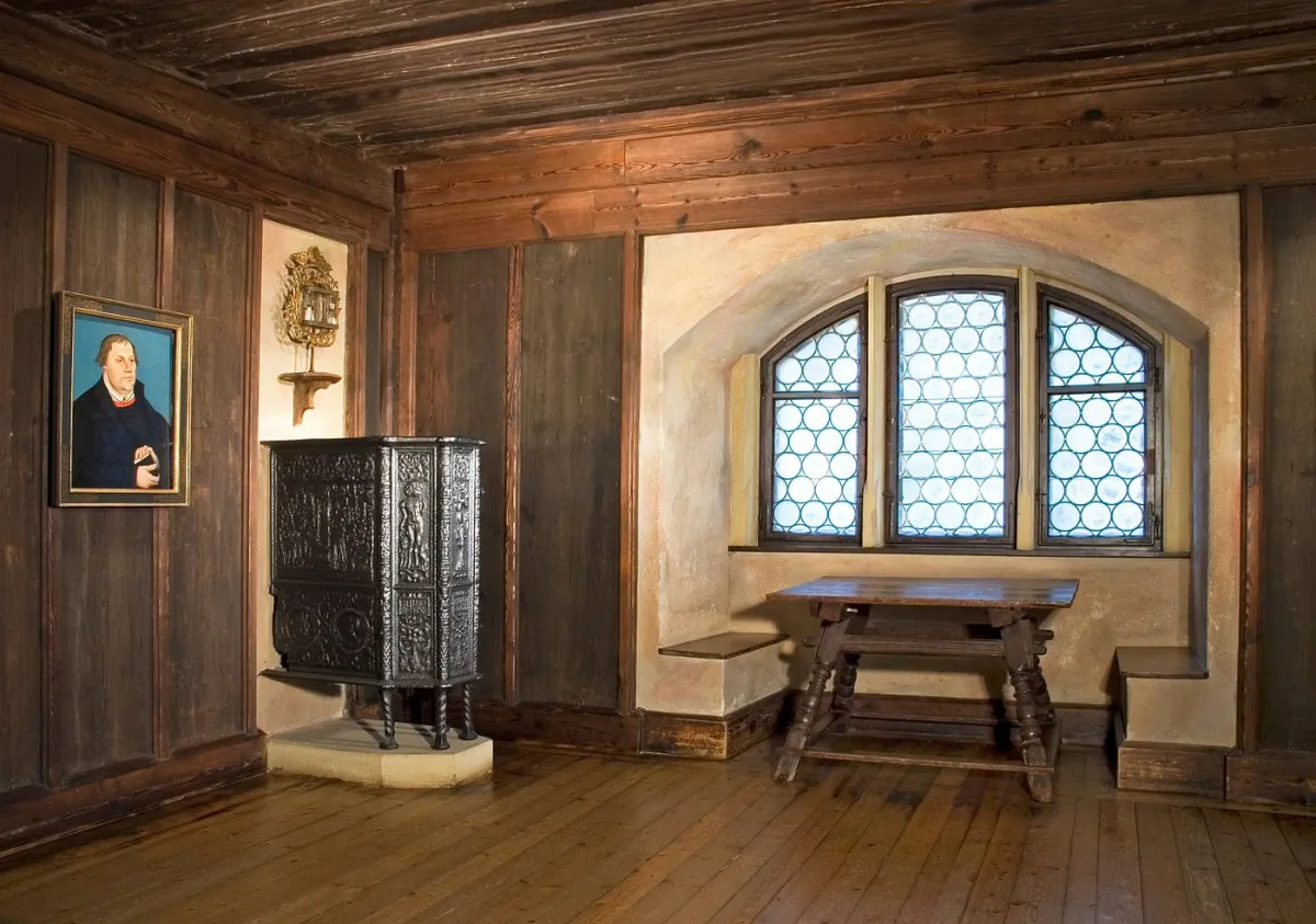 Historischer Raum mit Gemälde, Ofen und Tisch.