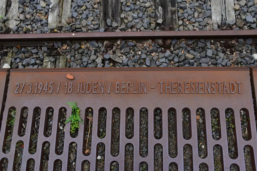 Gedenktafel mit Datum und Inschrift auf Bahngleisen.