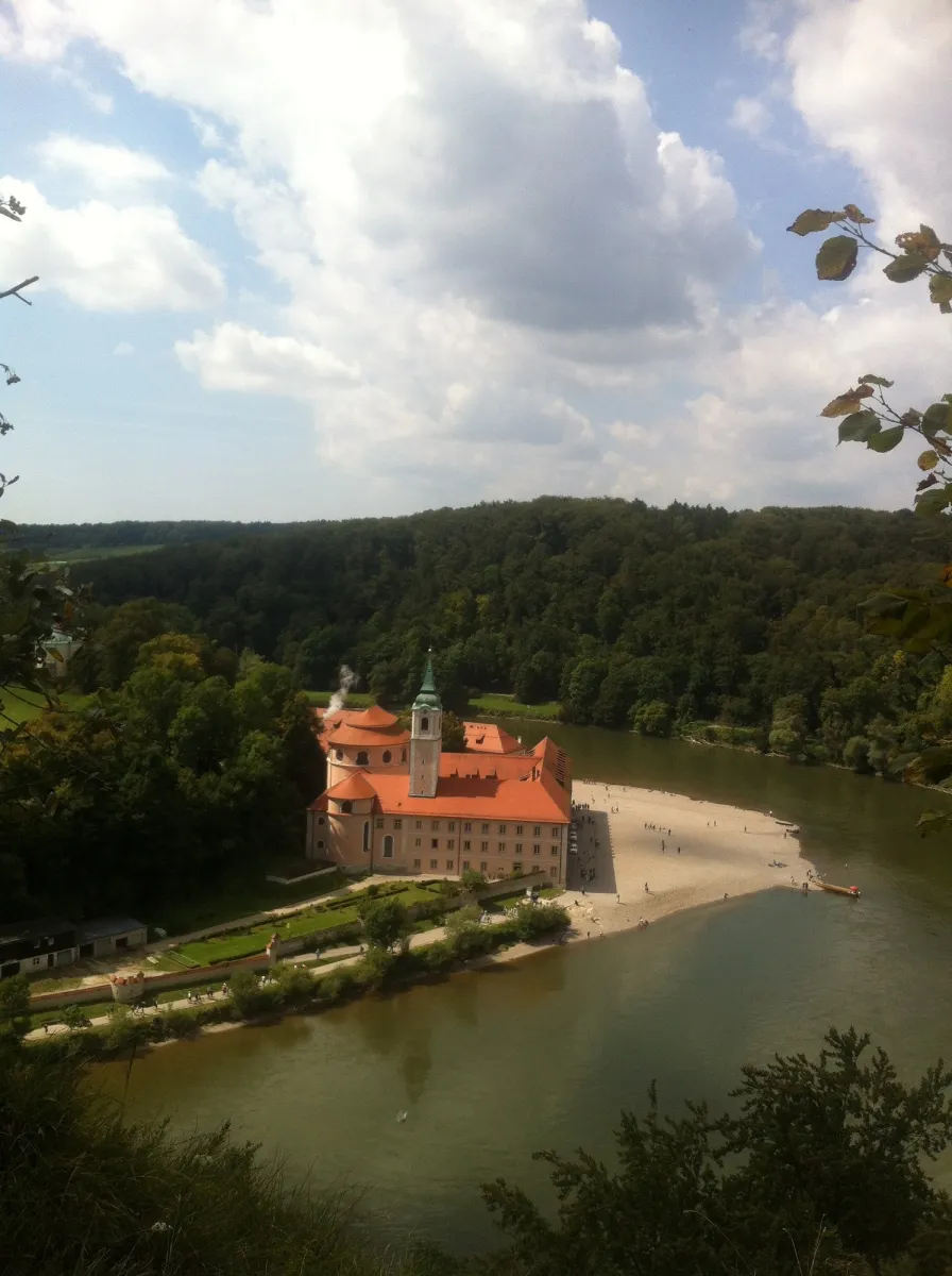Kloster an einem Flussufer mit Wald im Hintergrund