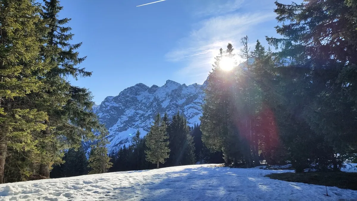 Verschneite Berglandschaft mit Sonne hinter Bäumen