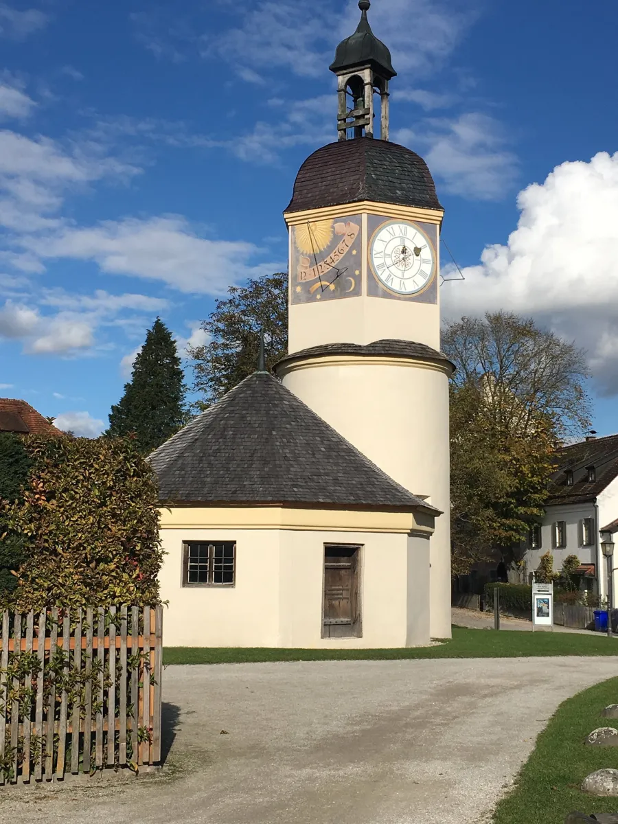 Historischer Uhrturm mit Sonnenuhr vor blauem Himmel.