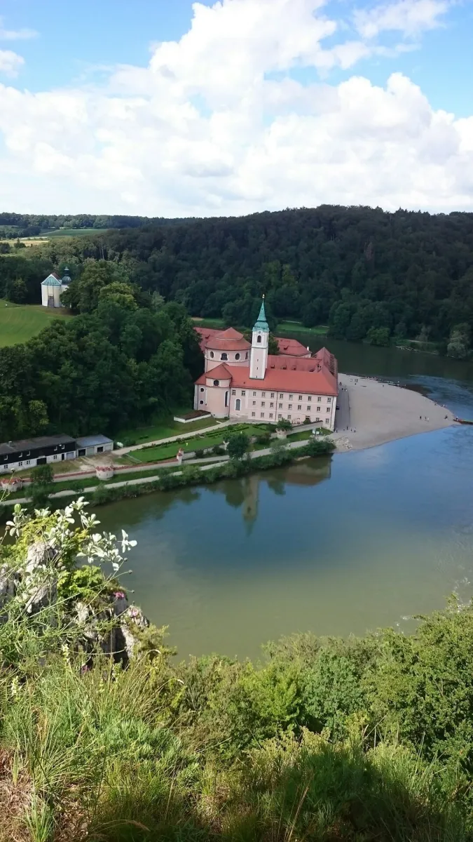 Kloster an einem Flussufer mit Wald im Hintergrund