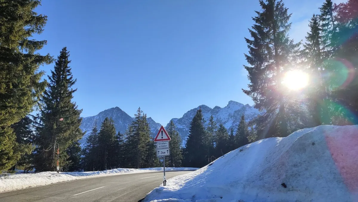 Verschneite Bergstraße mit Warnschild und Sonne im Hintergrund