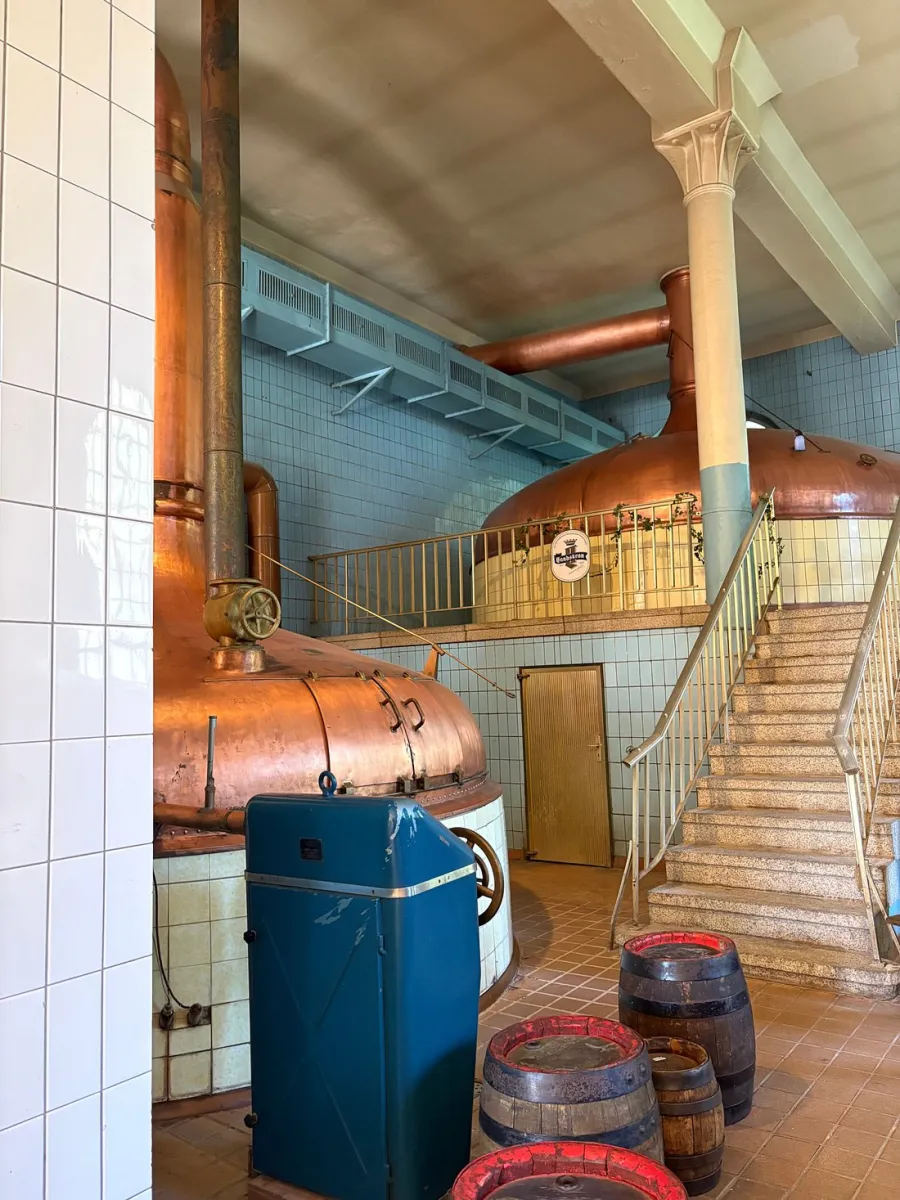 Innenansicht einer Brauerei mit Kupferkesseln und Fässern.
