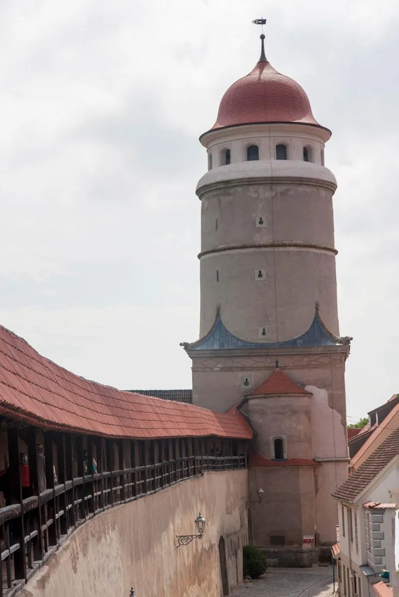 Runder Turm mit rotem Dach und angrenzender Stadtmauer.