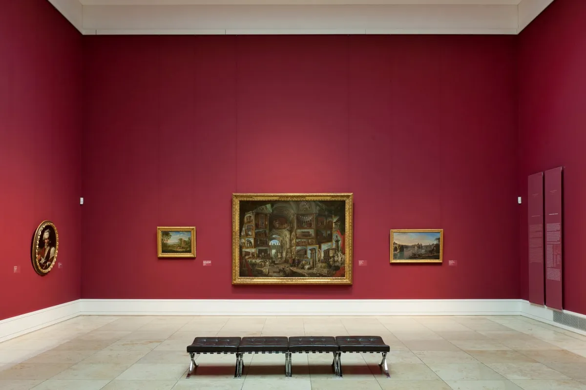 Kunstgalerie mit Gemälden an roten Wänden.