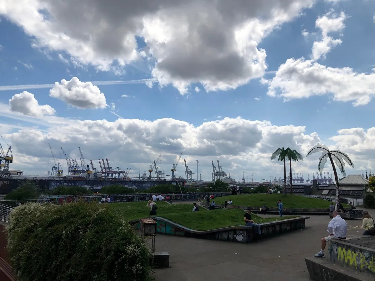 Park mit Menschen und Hafenkränen im Hintergrund.