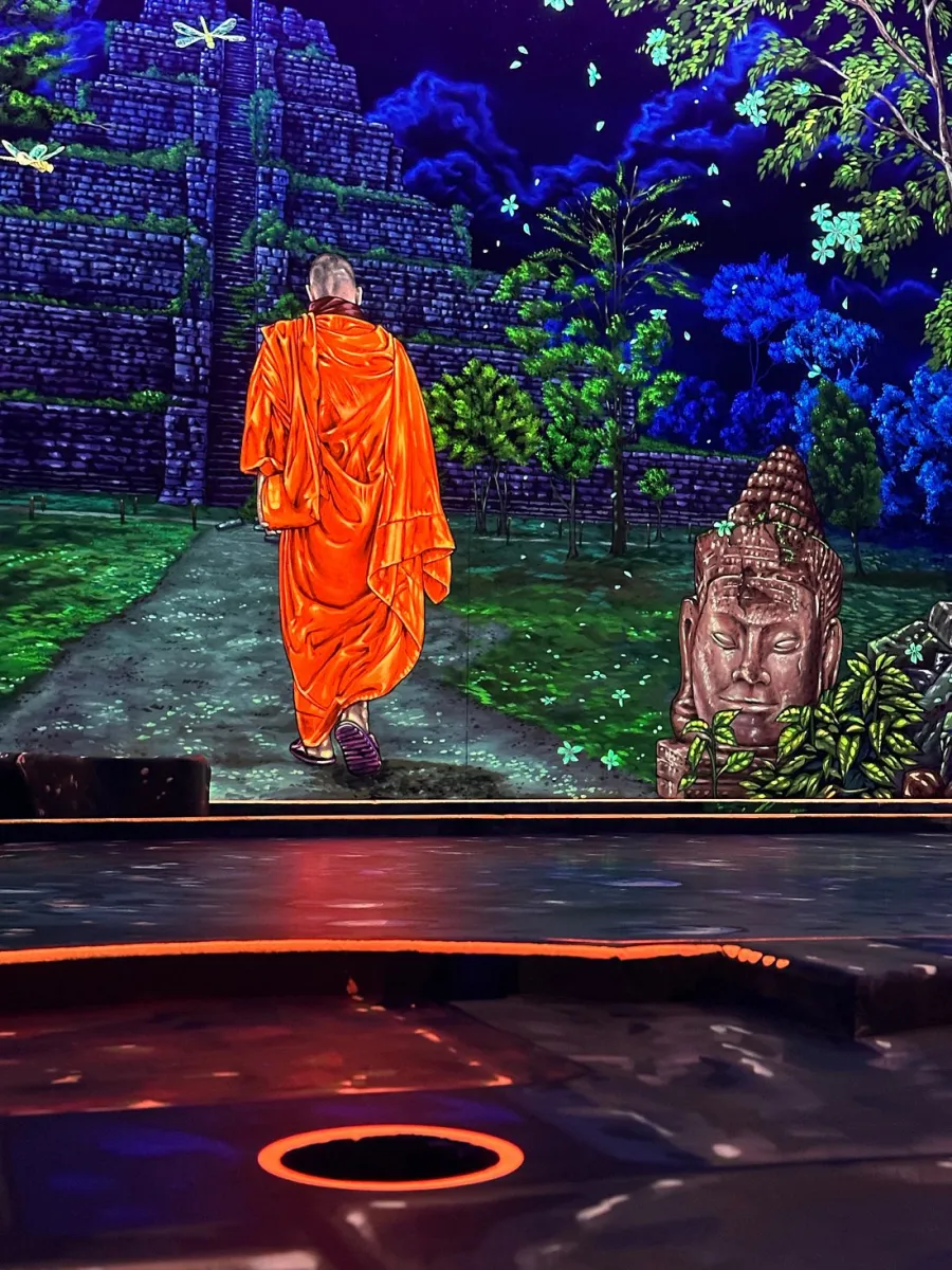 Mönch in orangefarbener Robe vor einem Tempelgemälde.
