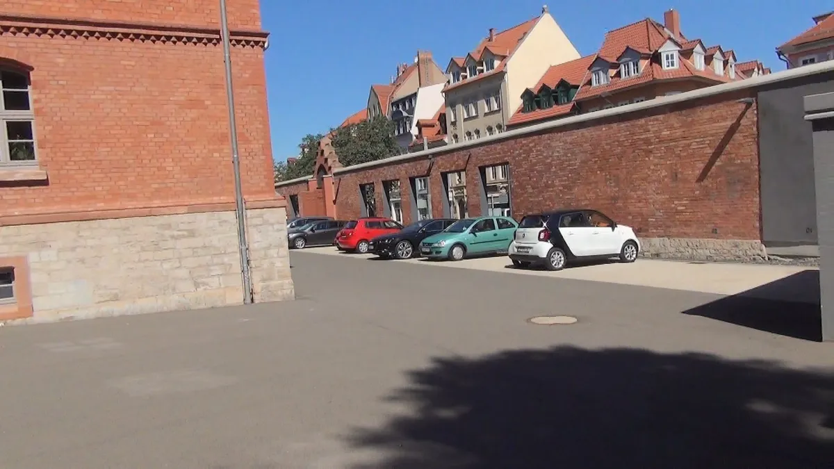 Parkplatz mit Autos neben roten Backsteingebäuden.