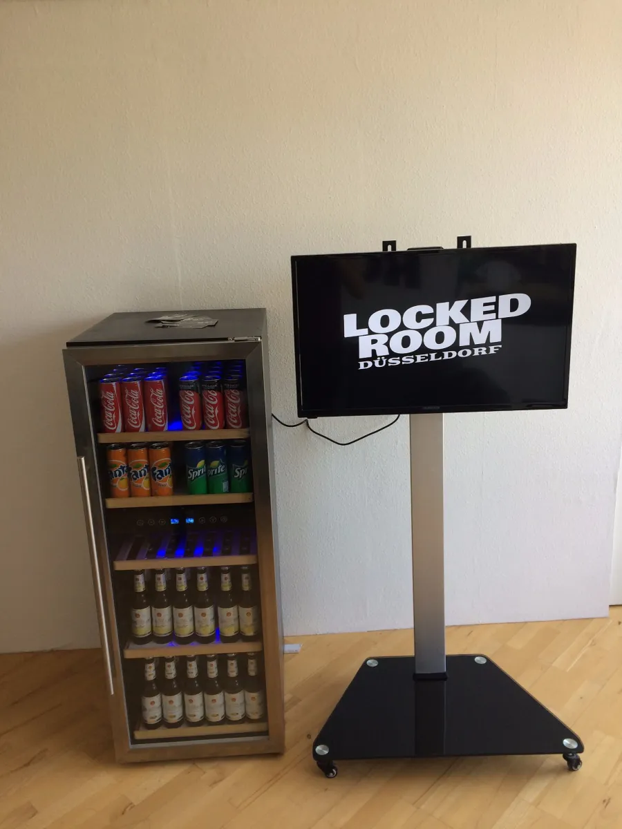 Getränkekühlschrank und Bildschirm mit 'Locked Room Düsseldorf'.