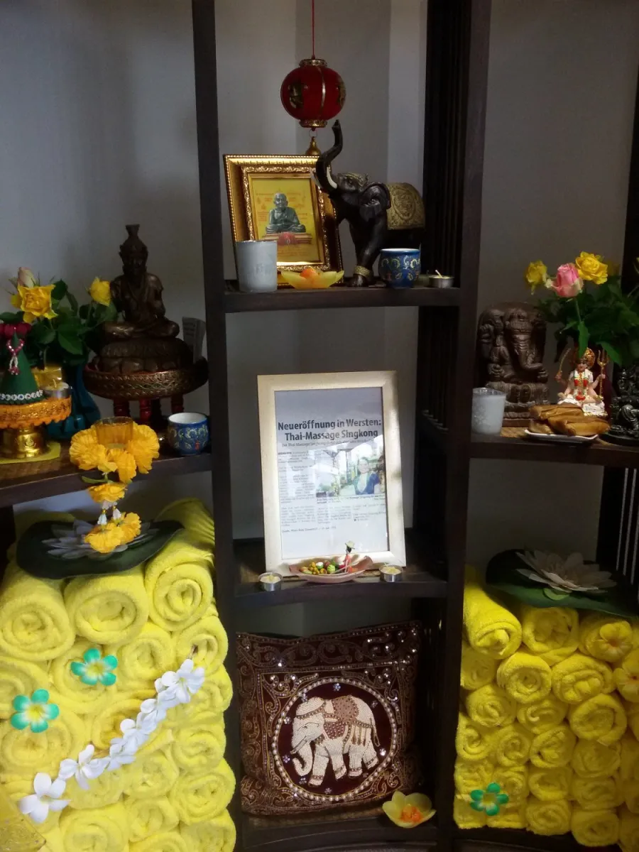 Regal mit buddhistischen Figuren und gelben Handtüchern.