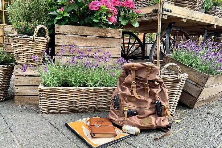 Brauner Rucksack neben Lavendel und Blumen in Körben.