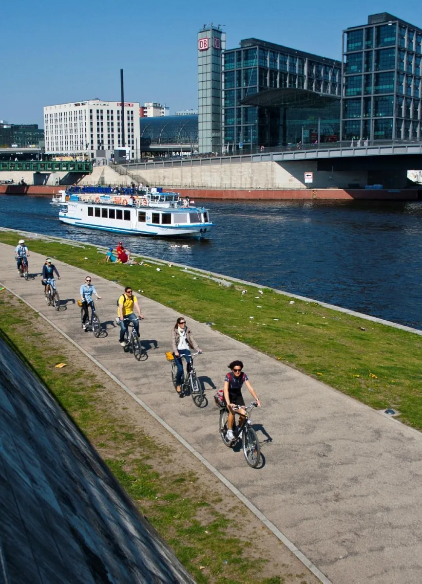Radfahrer am Flussufer vor einem modernen Gebäude.