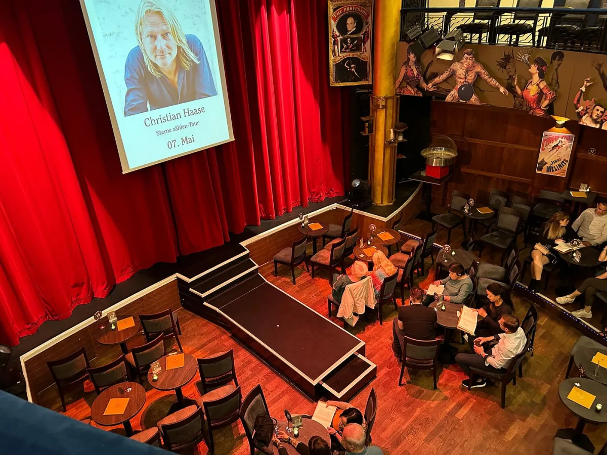 Theaterbühne mit rotem Vorhang und Publikum.