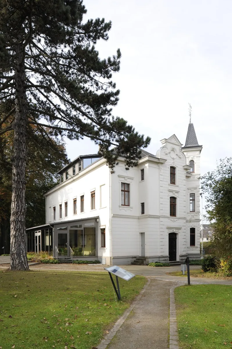 Weißes historisches Gebäude mit Turm und Garten.