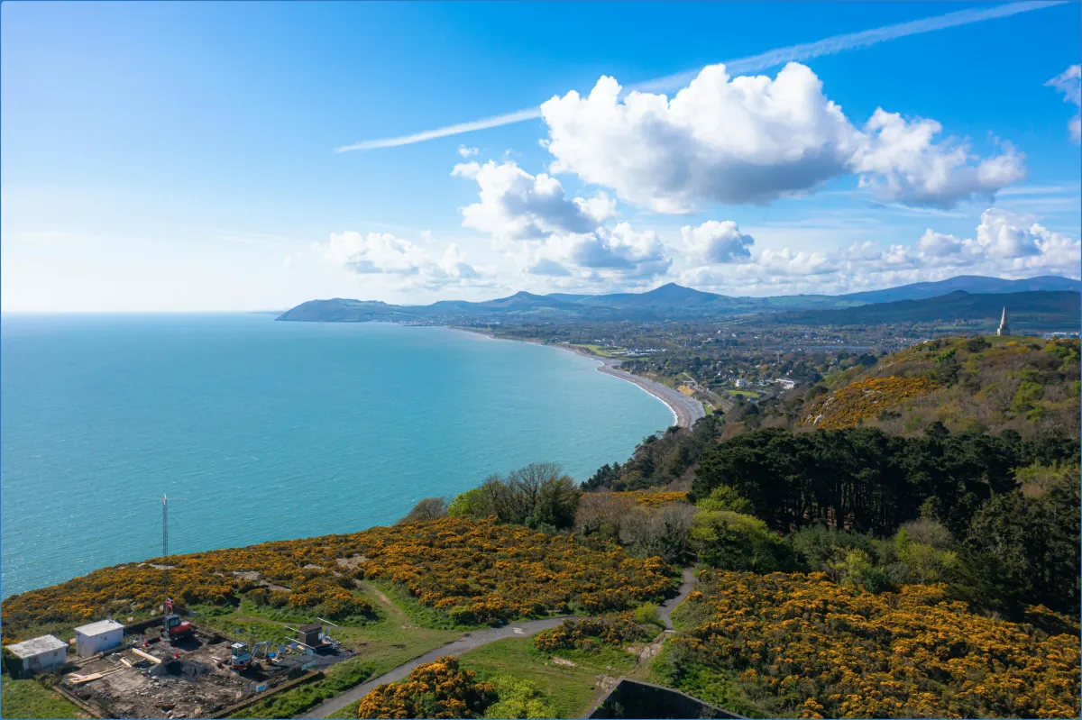 Coastal landscape with sea, hills, and cloudy sky.