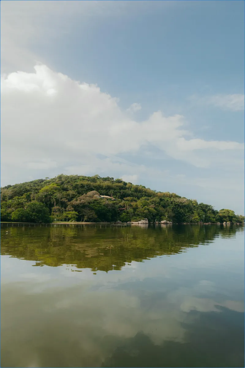 Lush green hill reflected in calm water under a blue sky.