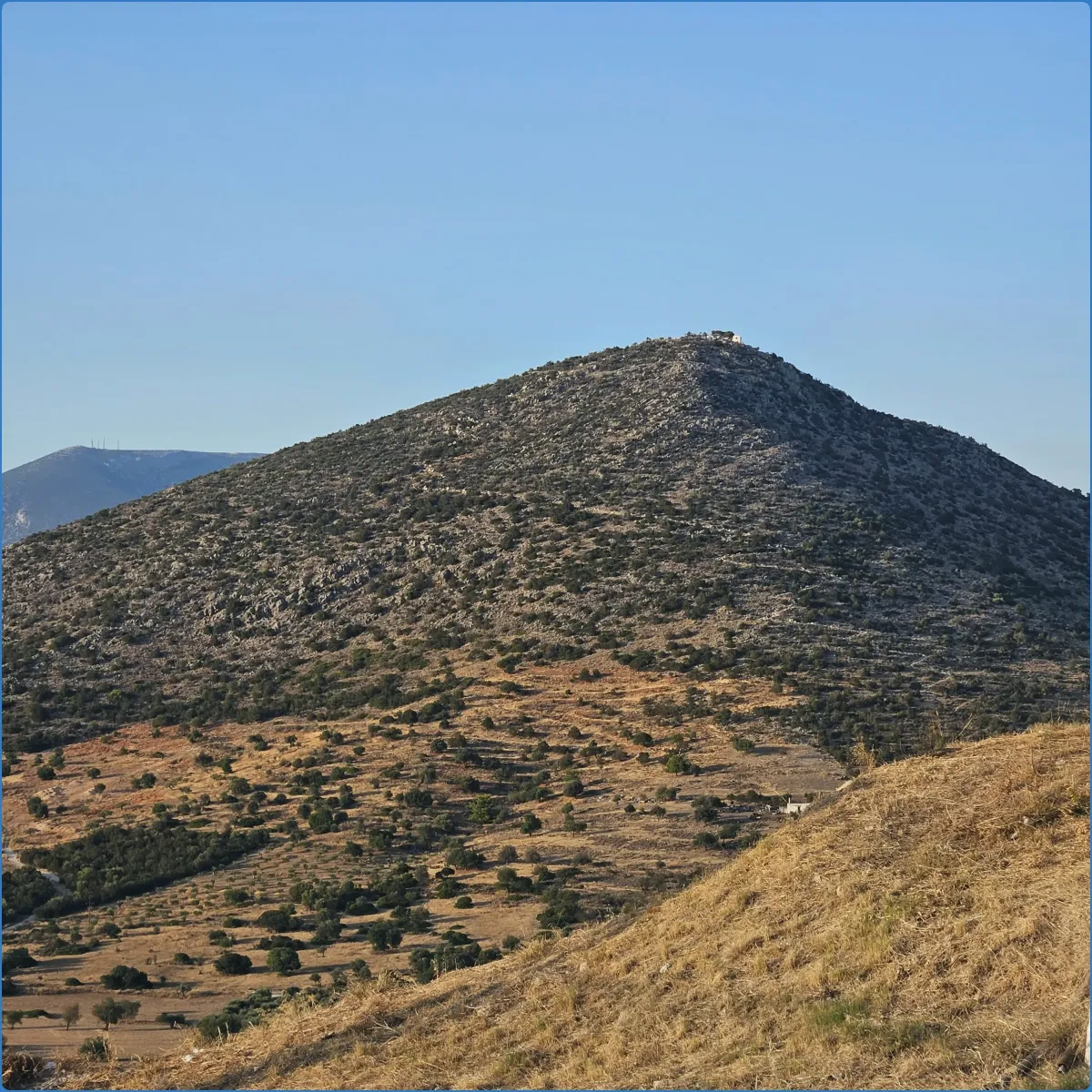 Rocky hill with sparse vegetation under a clear blue sky.