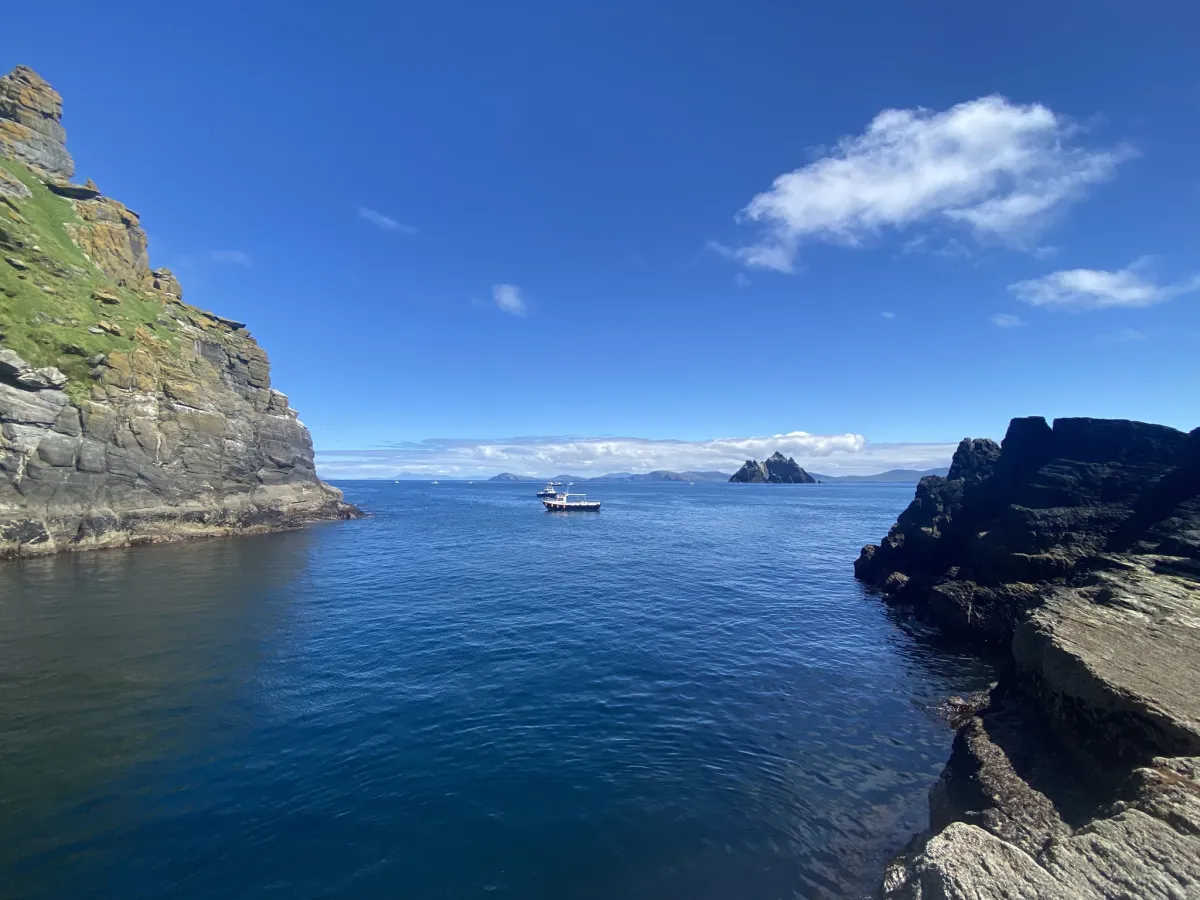 Boat on ocean near rocky cliffs and distant islands