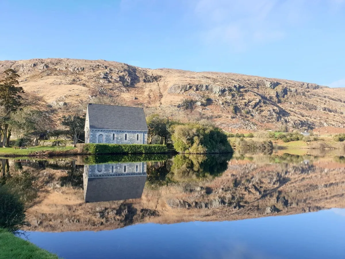 Stone chapel by a lake with mountain reflection.