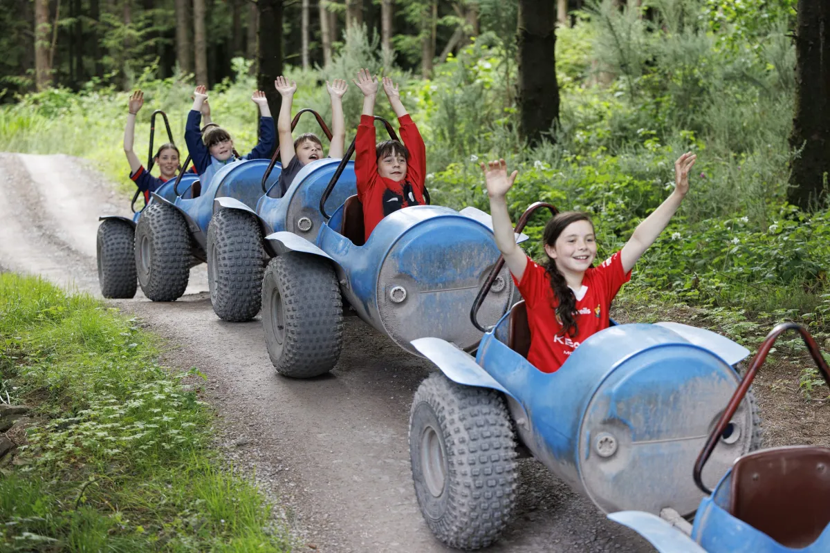 Children riding a blue caterpillar train in a forest.