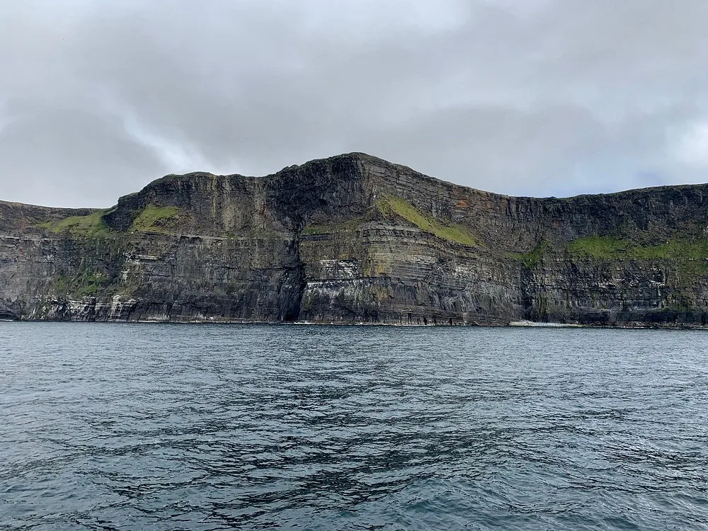 Cliffside view over the ocean under a cloudy sky.