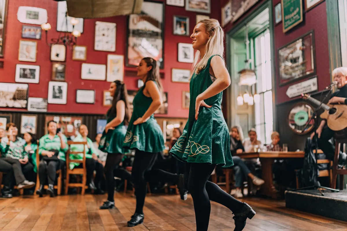 Three women performing Irish dance in a pub.