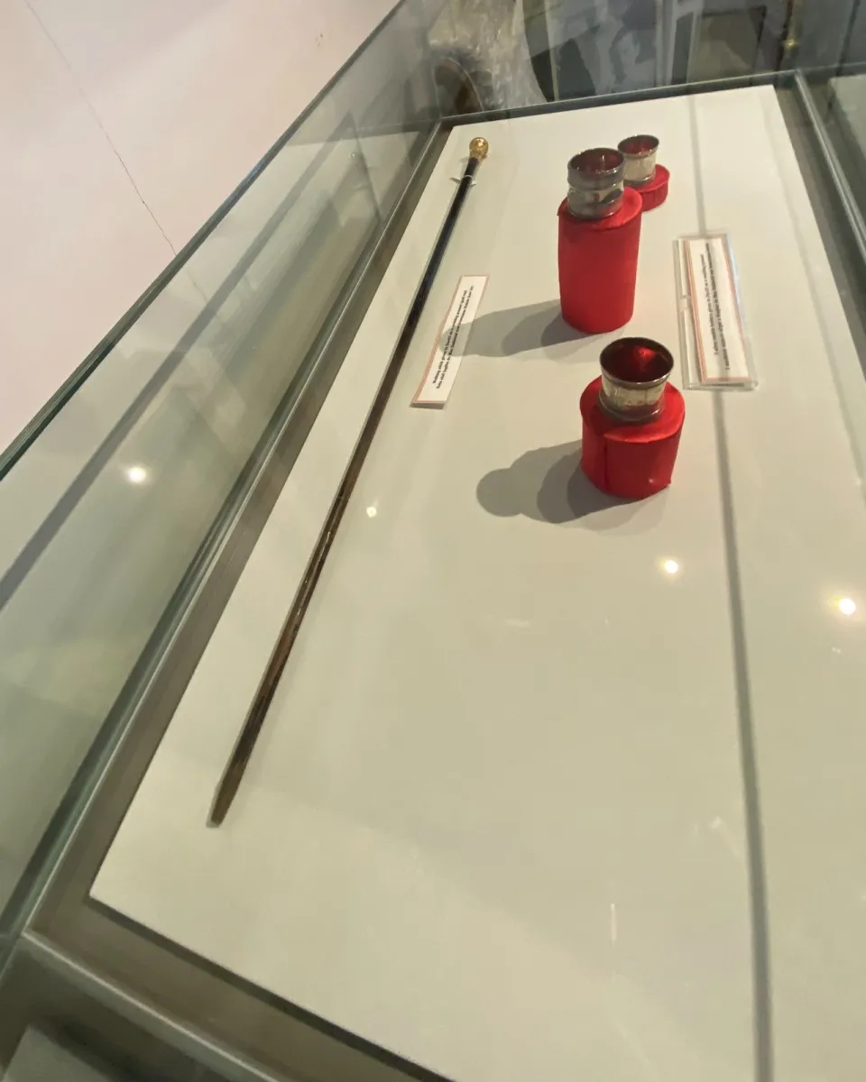 Display case with a ceremonial staff and red-capped items.
