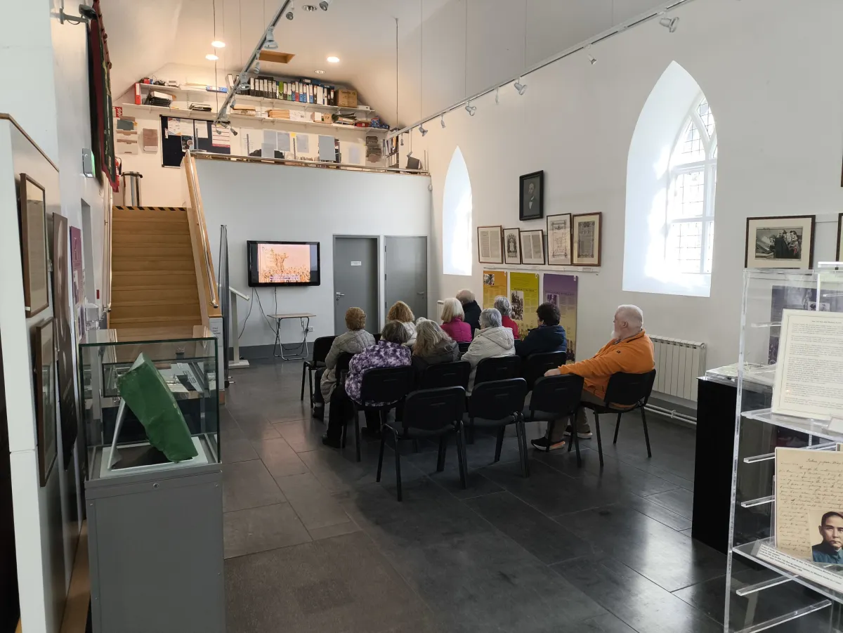 People seated in a museum watching a screen.