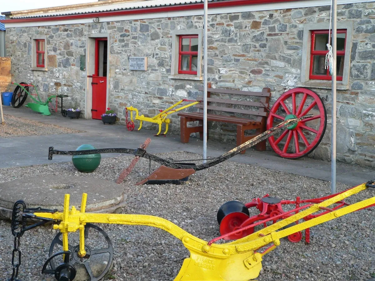 Colorful vintage farm equipment outside stone building.