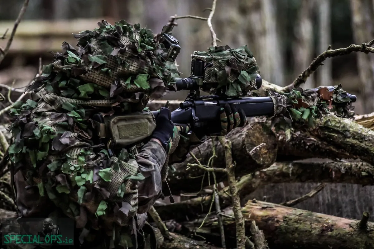 Camouflaged soldier aiming a rifle in a forest