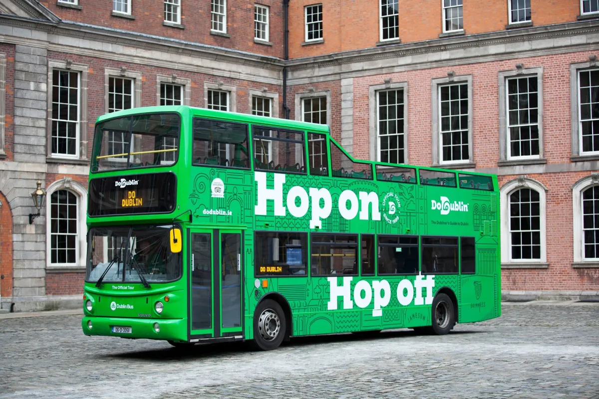 Green double-decker tour bus in front of a brick building