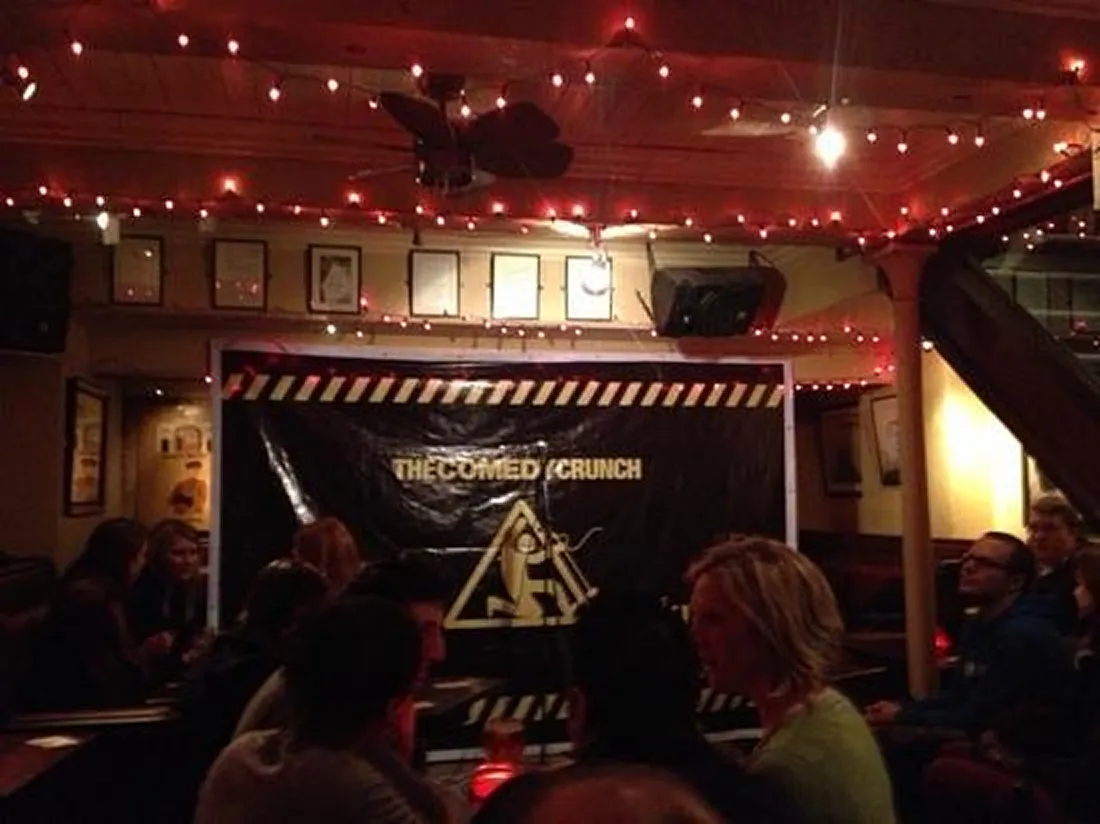 People seated in a dimly lit comedy club with a stage.