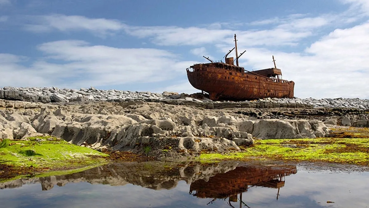 Rusty shipwreck on rocky shore with reflection in water