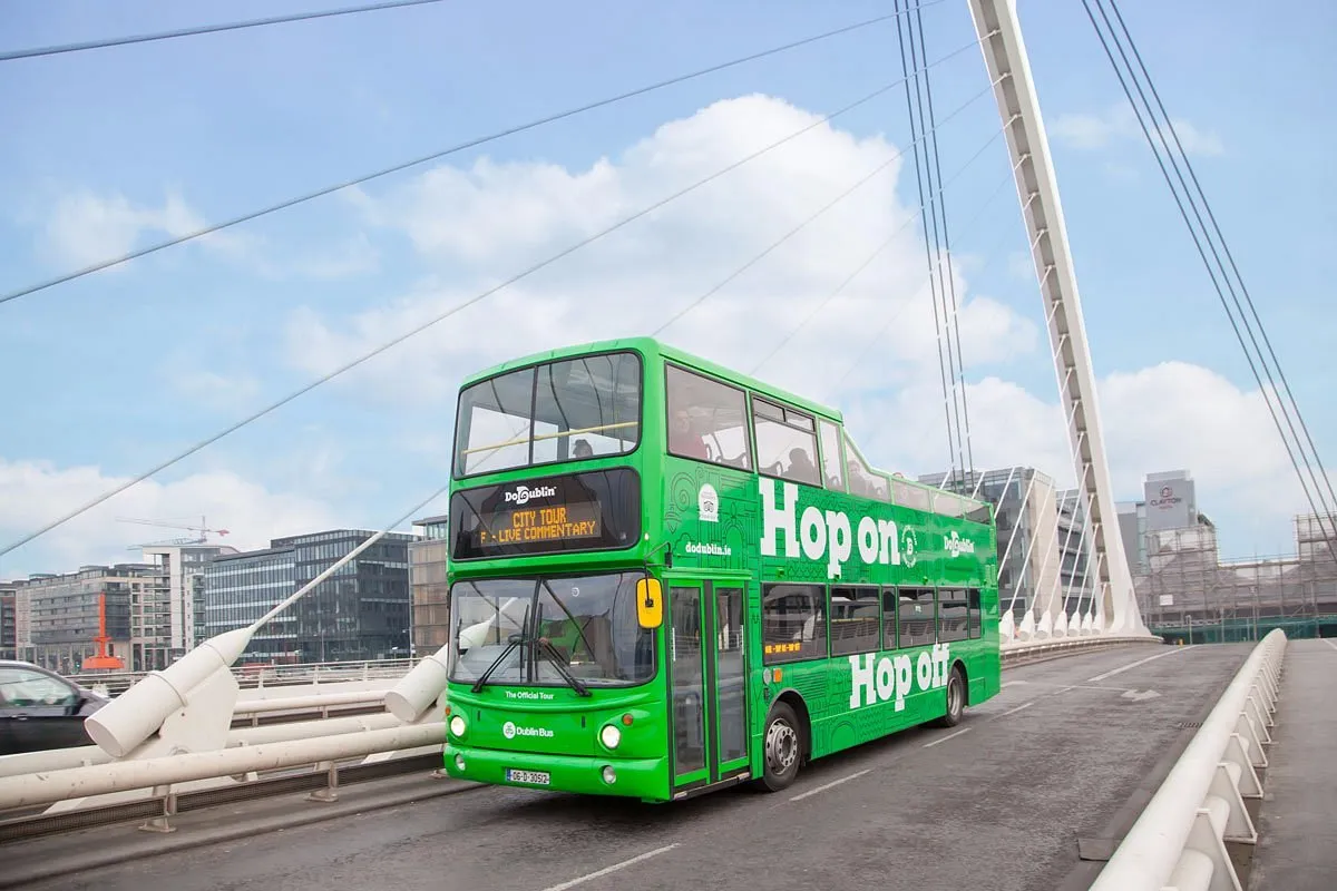 Green double-decker tour bus on a bridge.