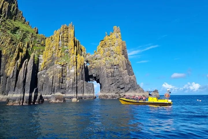 Boat near rocky sea arch under blue sky.