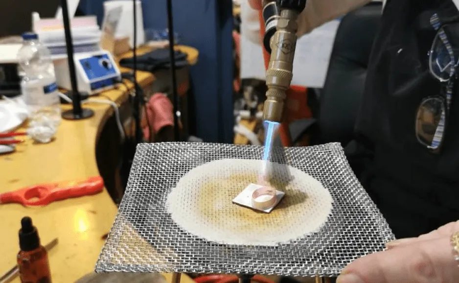Person using a blowtorch on metal piece on mesh.